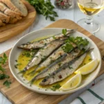 Close-up photo of marinated boquerones and grilled sardines served on a wooden board with fresh herbs and lemon slices.