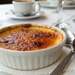 A close-up view of a crème brûlée with a golden, caramelized sugar crust and a spoon beside it, showcasing its rich texture.