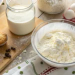 Bowl of kefir with freshly baked muffins on a wooden kitchen countertop, showcasing kefir’s role in baking.