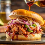 lose-up shot of a Memphis-style BBQ sandwich with pulled pork, BBQ sauce, pickles, and coleslaw on a wooden counter.